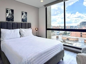 A bedroom with a large bed, a view of the city through a window, and two wall art pieces. - New Listing (Bogotá)