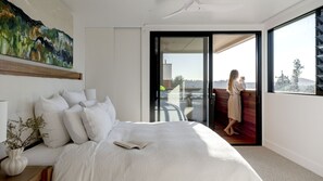 Ein Schlafzimmer mit einem großen Bett, einem Bild an der Wand und einem Balkon mit einer Person.