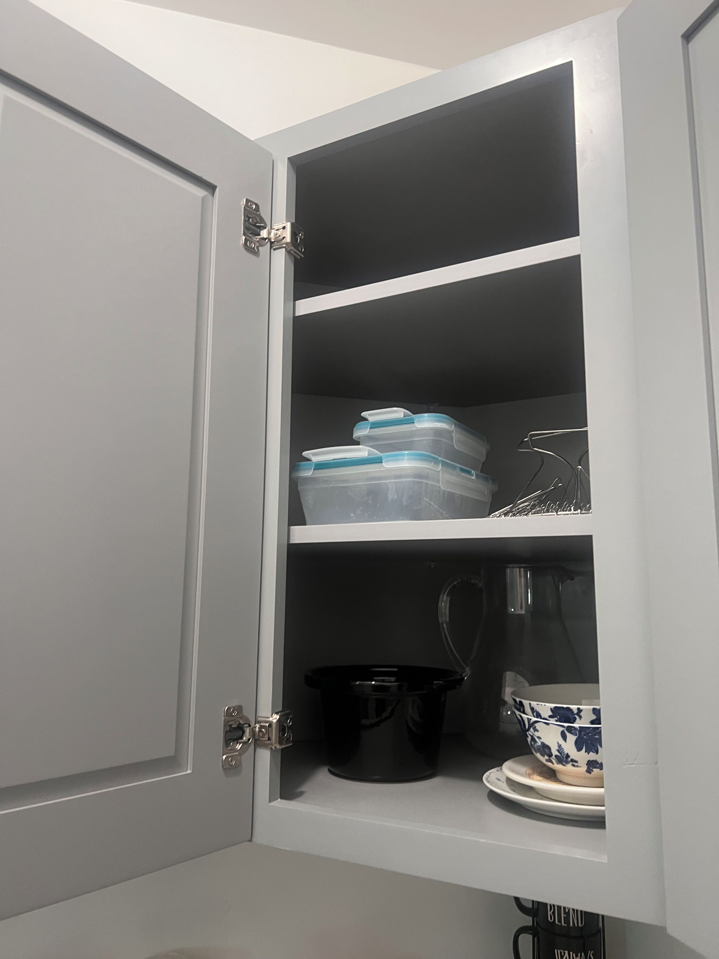 A white cabinet with three shelves, containing kitchenware and storage containers.