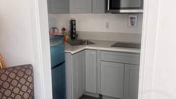 A compact kitchen with grey cabinets, a stainless steel sink, and a microwave.