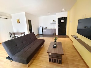 Un salon avec un canapé, une table basse, un téléviseur et, au fond, un coin cuisine.