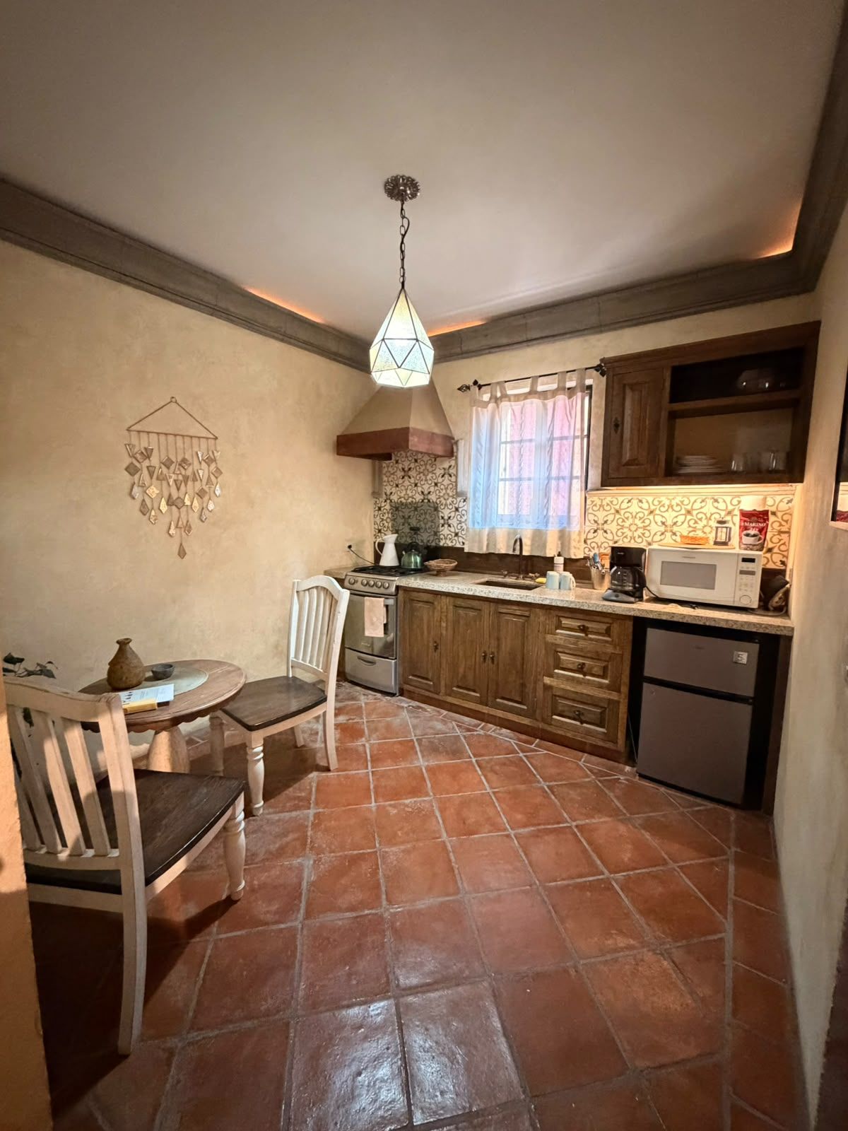 A kitchen with a tiled floor, wooden cabinets, a stove, a microwave, and a hanging light fixture.