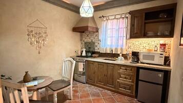 A kitchen with a tiled floor, wooden cabinets, a stove, a microwave, and a hanging light fixture.