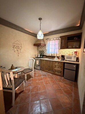 Cozinha com piso ladrilhado, armários de madeira, fogão, micro-ondas e luminária pendente.