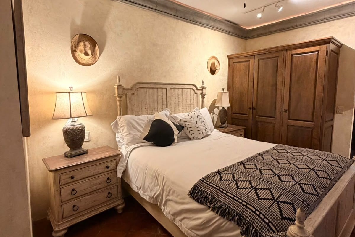 Quarto com cama, mesas de cabeceira, ventilador de teto e armários de madeira.