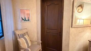 A room with a wooden door, a chair with a striped cushion, a small rug, and a wall-mounted mirror.
