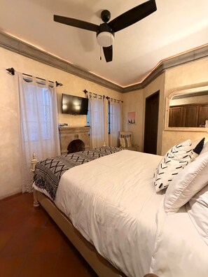Quarto com cama, ventilador de teto, televisão e lareira.