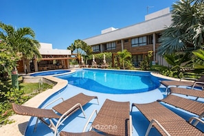A swimming pool with lounge chairs, surrounded by greenery and a building with large windows.