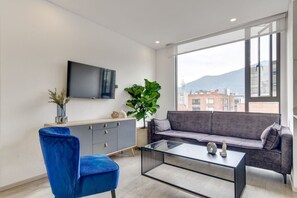 A modern living room with a sofa, a blue chair, a coffee table, and a TV mounted on the wall. - New Listing (Bogotá)