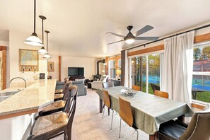 A spacious living area with a kitchen, dining table, and a large window offering a view of a tennis court. - Aspen Village McCall Condo | Pools, Gym, Hot Tub (McCall)