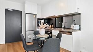 A modern kitchen with a dining area, featuring a refrigerator, stove, sink, and a small island with a toaster. - Platinum Views Southbank (Southbank)