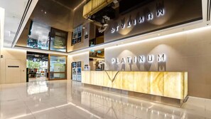 Eine moderne Hotelhalle mit einer 'PLATINUM' Rezeption, einer Glasfassade und einem sauberen, spiegelnden Boden.