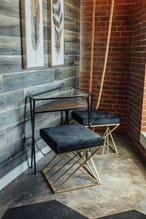 Een hoekje met een metalen tafel, twee gestoffeerde krukken, een bakstenen muur en een touw.