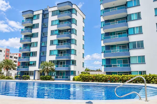 A modern multi-story residential building with balconies, a swimming pool, and a clear blue sky. - New Listing (Tonsupa)