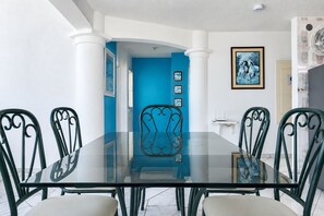 Un comedor con una mesa de vidrio y sillas de metal, una pared azul decorativa y cuadros en la pared.