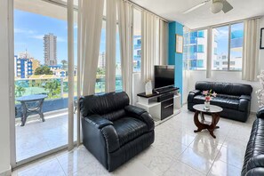 A modern living room with a flat-screen TV, two black leather sofas, a small round coffee table, and a balcony with a table and chairs. - New Listing (Tonsupa)