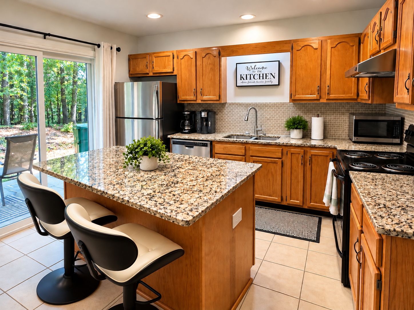 A modern kitchen with wooden cabinets, stainless steel appliances, a granite countertop, and a view of greenery outside.