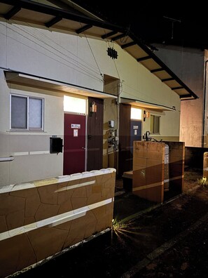 Un edificio con puerta roja, una ventana y una puerta con un cartel. Se observan estructuras de madera y una viga metálica en el techo.