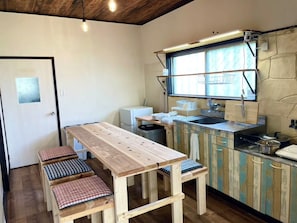 A compact kitchen with a wooden table and benches, a window with a view, and a stone wall.