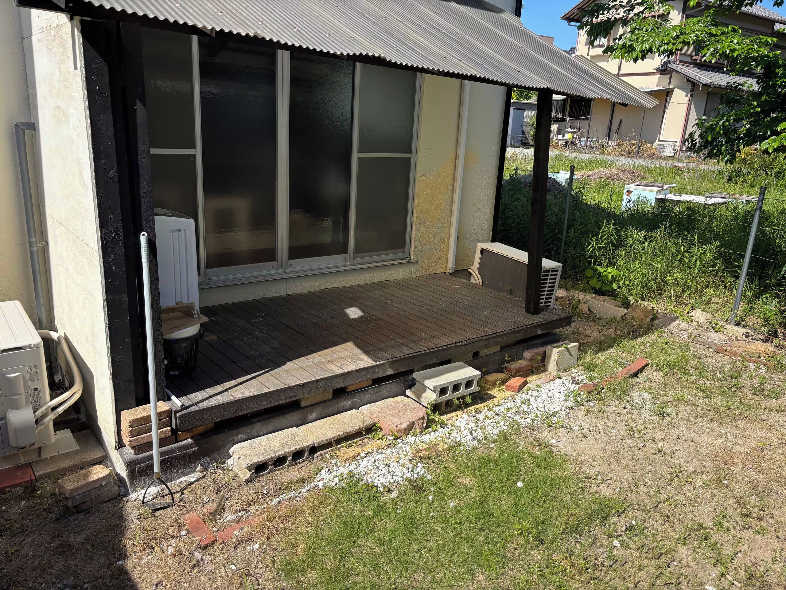 A residential building with a wooden deck, a sliding glass door entrance, and a small outdoor seating area.