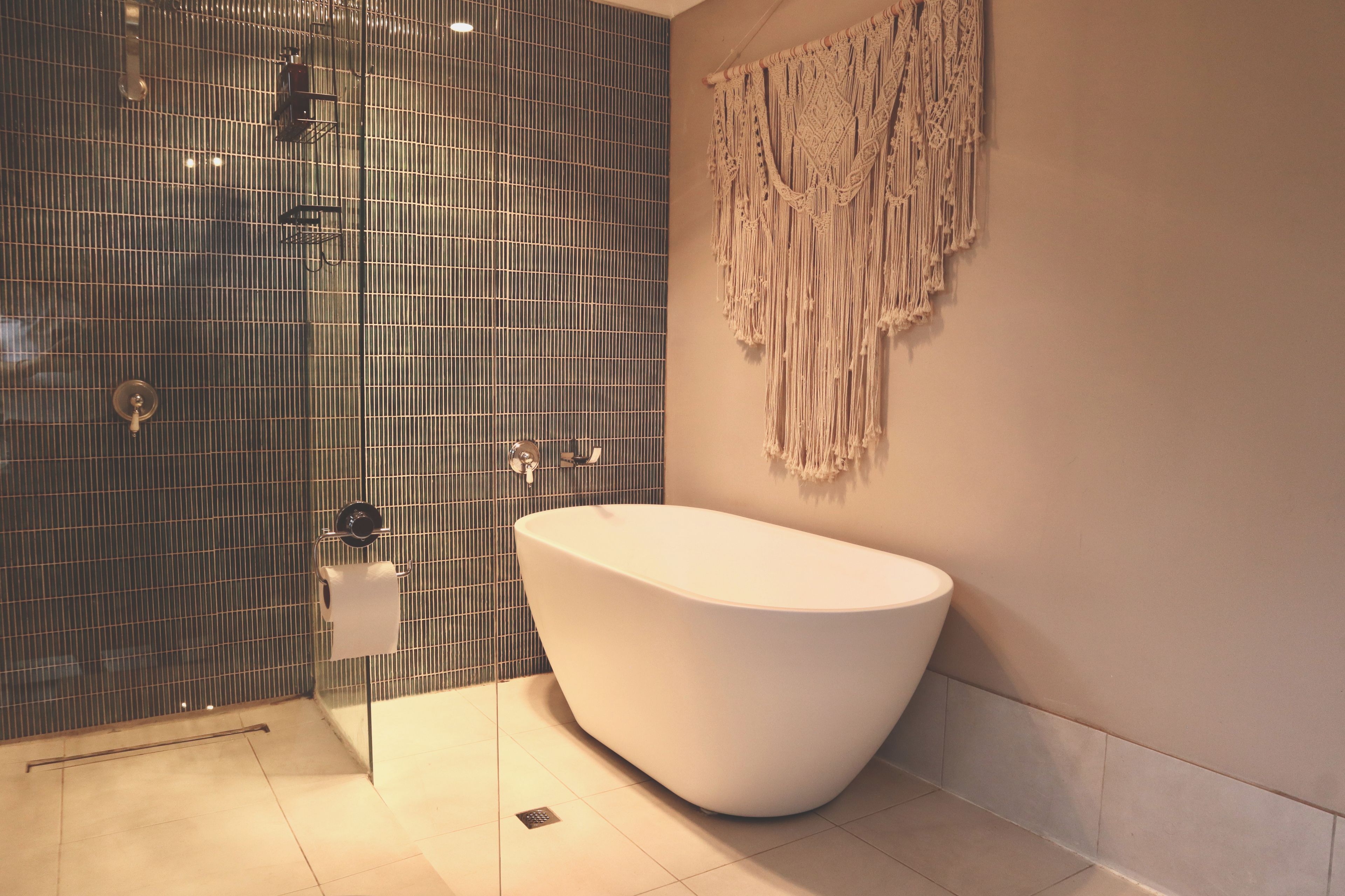Une salle de bain avec une baignoire sur pieds, une douche avec une porte en verre et une décoration murale en macramé.