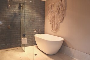 Un baño con una bañera independiente, una ducha con puerta de vidrio y un colgador de macramé en la pared.