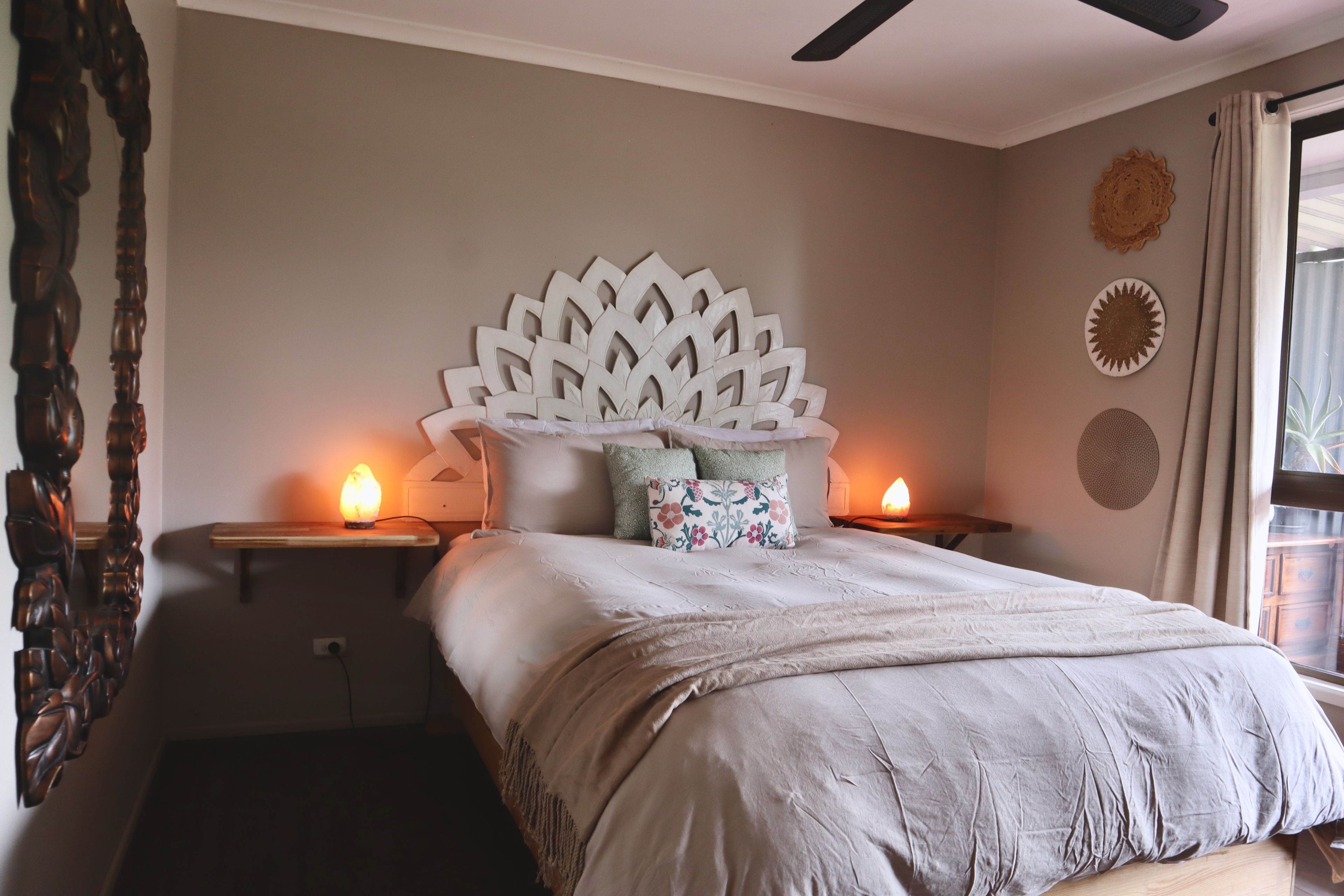 A bedroom with a bed, two nightstands, a decorative headboard, and wall decor.