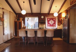 A kitchen with a wooden bar, four stools, a refrigerator, and a clock on the wall.