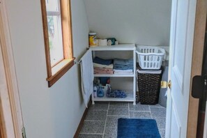 Un cuarto de lavandería con estantes, una cesta y productos de limpieza.