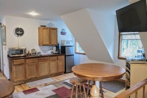 Eine kleine Küche mit Holzschränken, einer Mikrowelle und einem Essbereich mit Hocker.