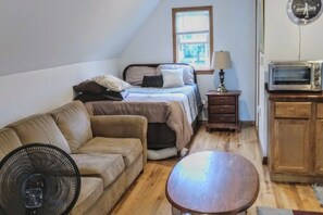 Ein gemütlicher Raum mit Bett, einer Schlafcouch, einem kleinen Tisch, einem Ventilator, einer Lampe und einer Mikrowelle.