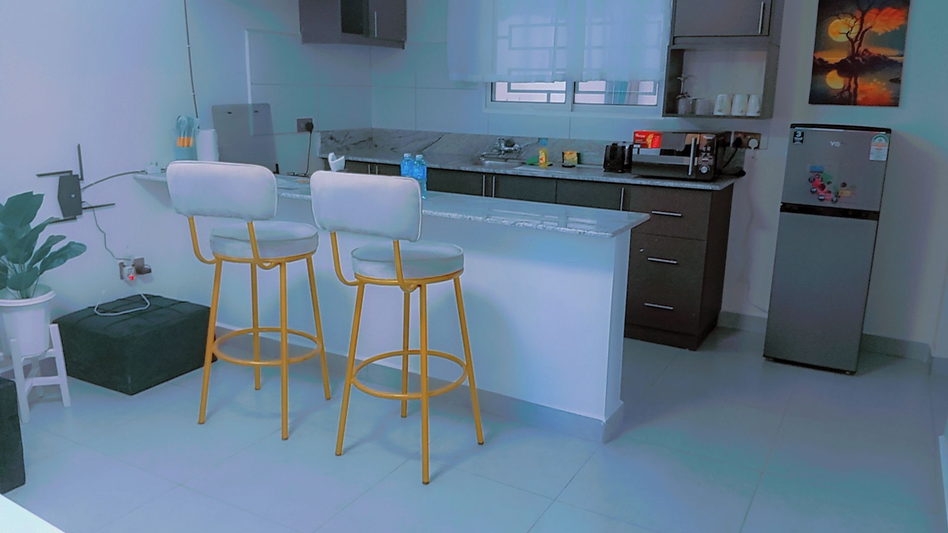 A modern kitchen with two bar stools, a refrigerator, and a countertop with various items.