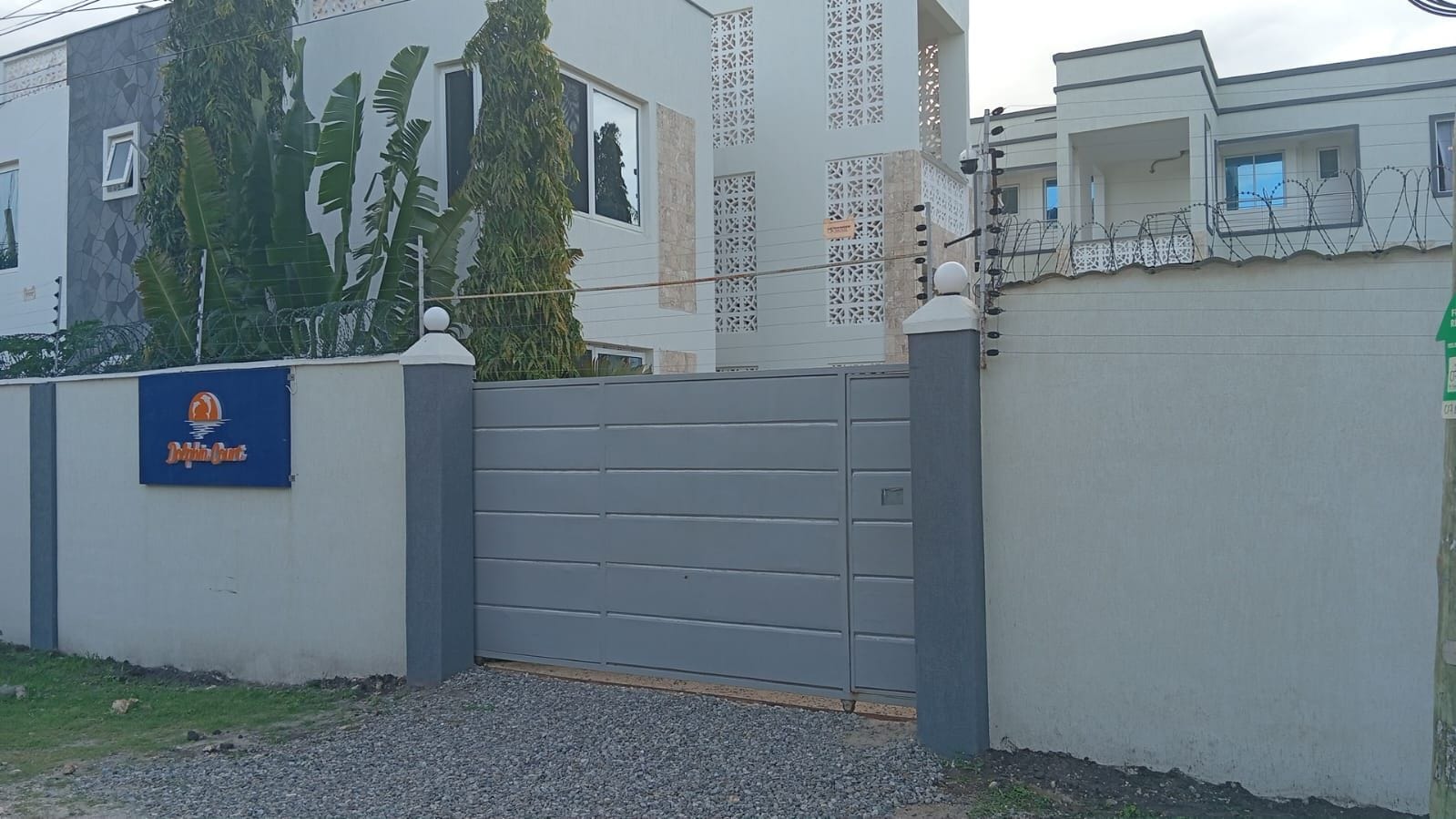 A gated entrance with a blue sign, a grey gate, and a white wall with a decorative pattern.