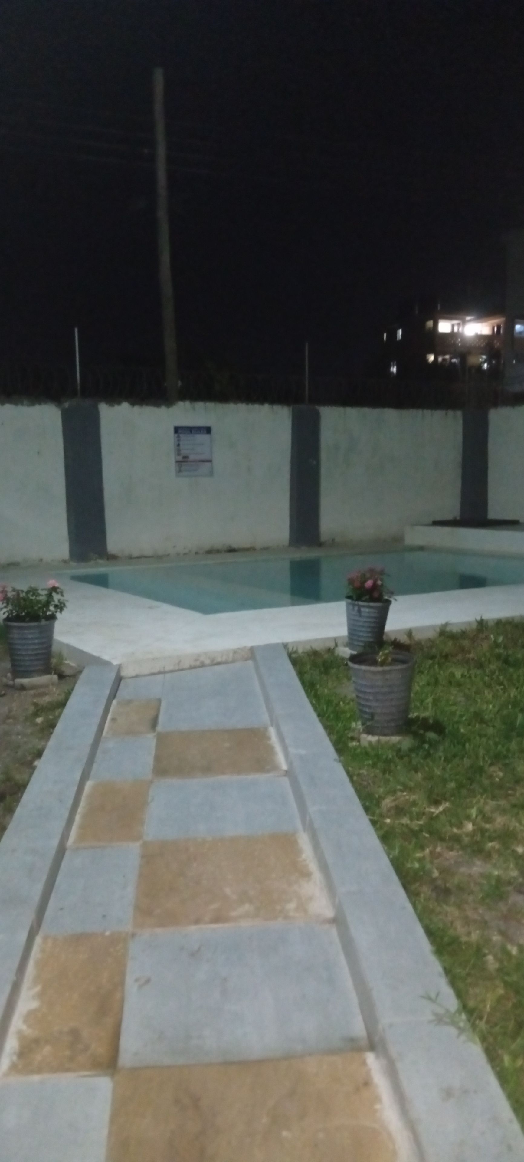 A nighttime outdoor area with a swimming pool, a paved walkway, and potted plants.