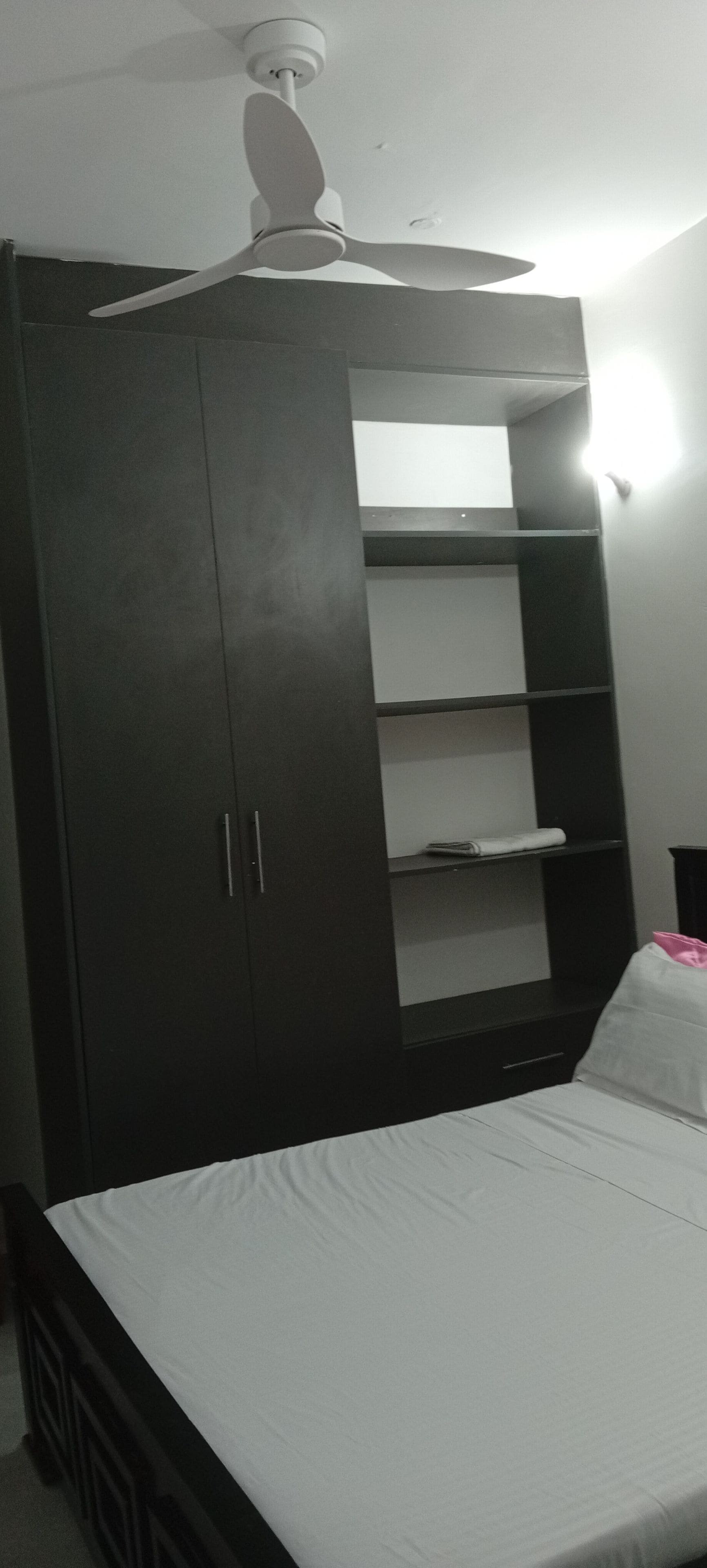 A bedroom with a bed, a wardrobe, and a ceiling fan.