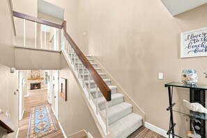 Eine Treppe mit Holzgeländer und weißen Spindeln, die zu einer Zwischenebene mit Teppich und Wanddeko führt.