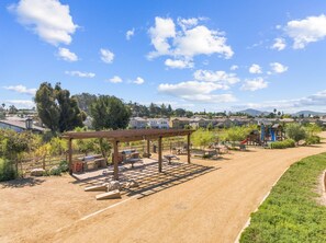 Un parque con zona de barbacoa, mesas de picnic y parque infantil.