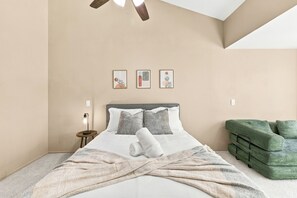 Quarto com cama, mesa de cabeceira, sofá verde e três quadros na parede.