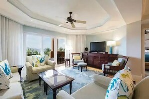 Ein Hotelzimmer mit Wohnbereich, ausgestattet mit einer Couch, Sesseln, einem Couchtisch, einem Fernseher und einem Deckenventilator.