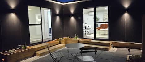 A modern outdoor seating area with a table and chairs, surrounded by dark walls and large windows.