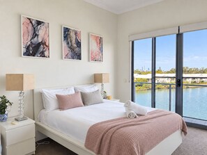 Un dormitorio con una cama grande, dos lámparas de noche y vista a un cuerpo de agua a través de una puerta corrediza de vidrio.