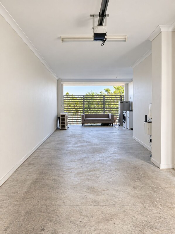 A spacious room with a concrete floor, a large window with a view of greenery, and a sofa. - Waterfront 2BR Townhouse | Balcony & parking (Carrara)
