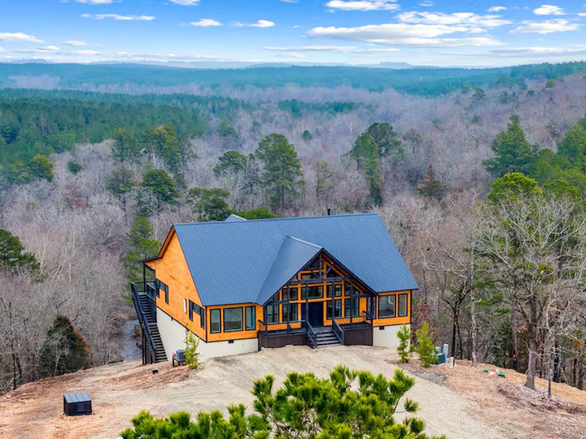 A cabin with a sloped roof, large windows, and a staircase leading to the entrance.