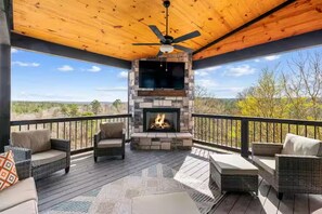 A covered outdoor deck with a stone fireplace, wicker furniture, and a view of the landscape. - Panoramic views, Creek, Total Privacy, 1 of a Kind (Broken Bow)