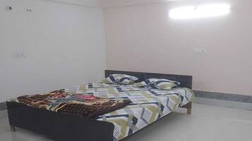 Una cama con colcha y almohadas estampadas, cabecera oscura y pared blanca con interruptor de luz.