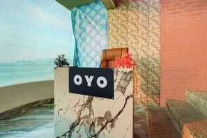 Een marmeren receptiebalie met een bord waarop 'OYO' staat, in een hotelhal met behang met een patroon en een blauw gordijn.