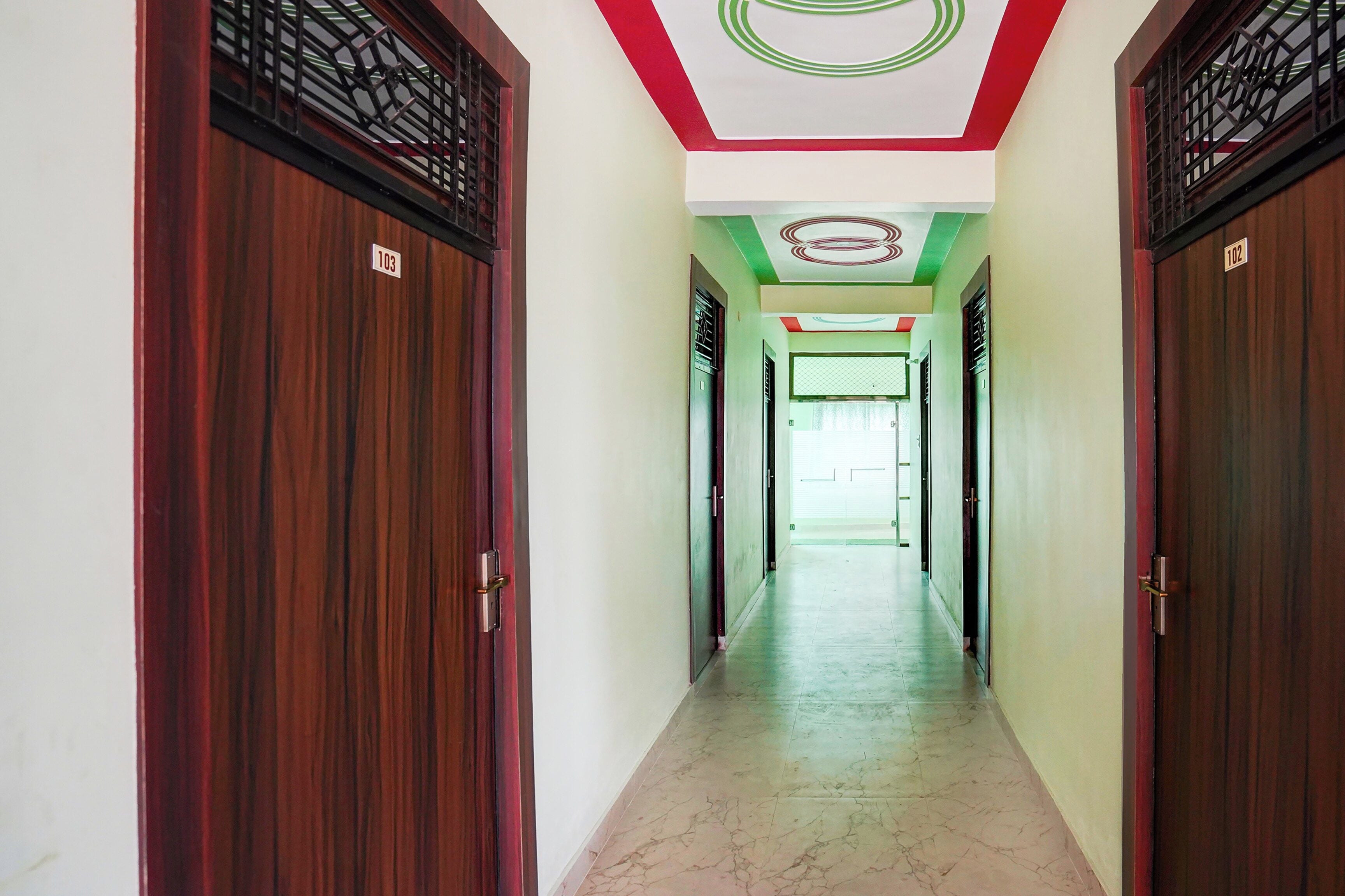 A corridor with wooden doors, numbered 103 and 102, leading to a room with a green and white ceiling.
