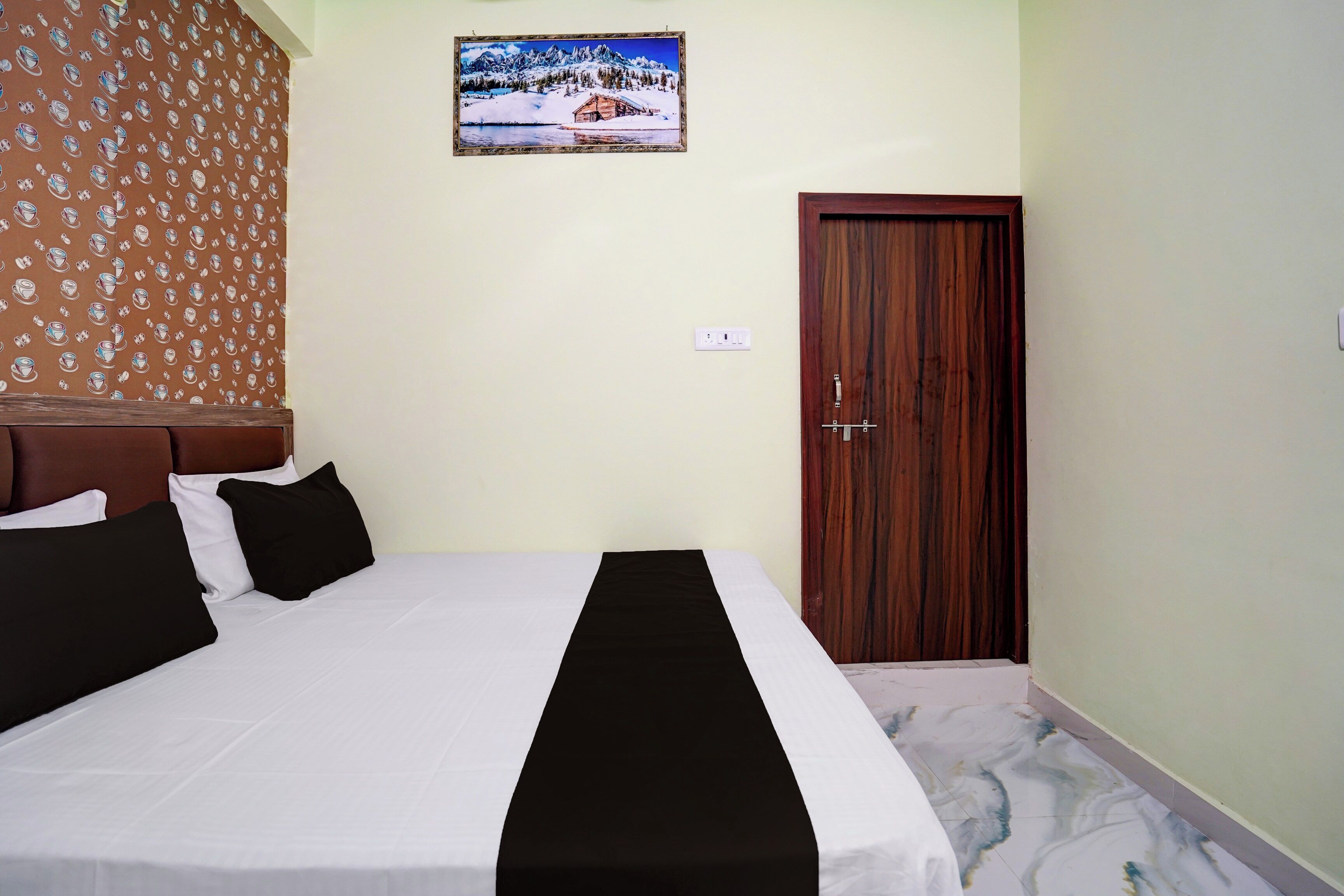 Une chambre d’hôtel avec un lit, une porte en bois, un tableau accroché au mur et un rideau à motifs.