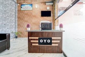 Un mostrador de recepción con un cartel que dice 'OYO', un cuadro con caballos y dos plantas en macetas.