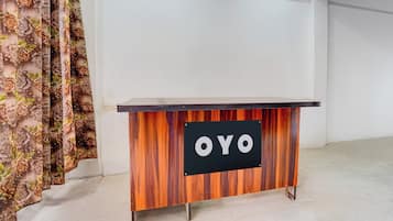 A wooden desk with a black panel displaying 'OYO' in white letters, situated in a room with a plain white wall and a curtain with a floral pattern.